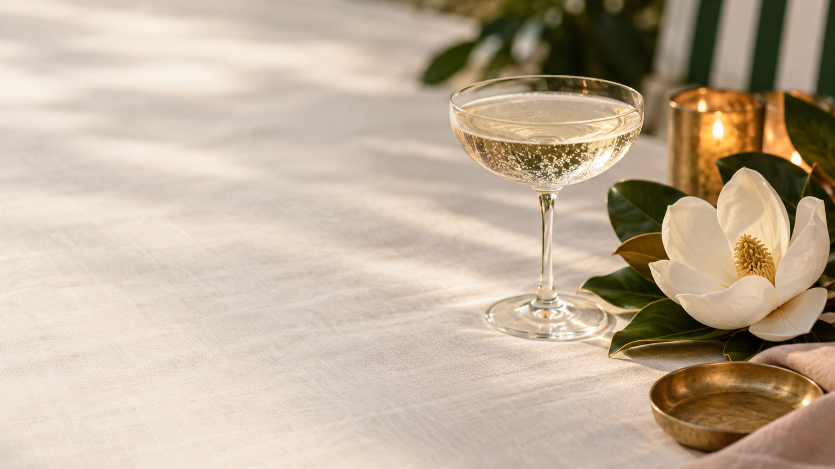 Champagne coupe beside a magnolia blossom on a linen table